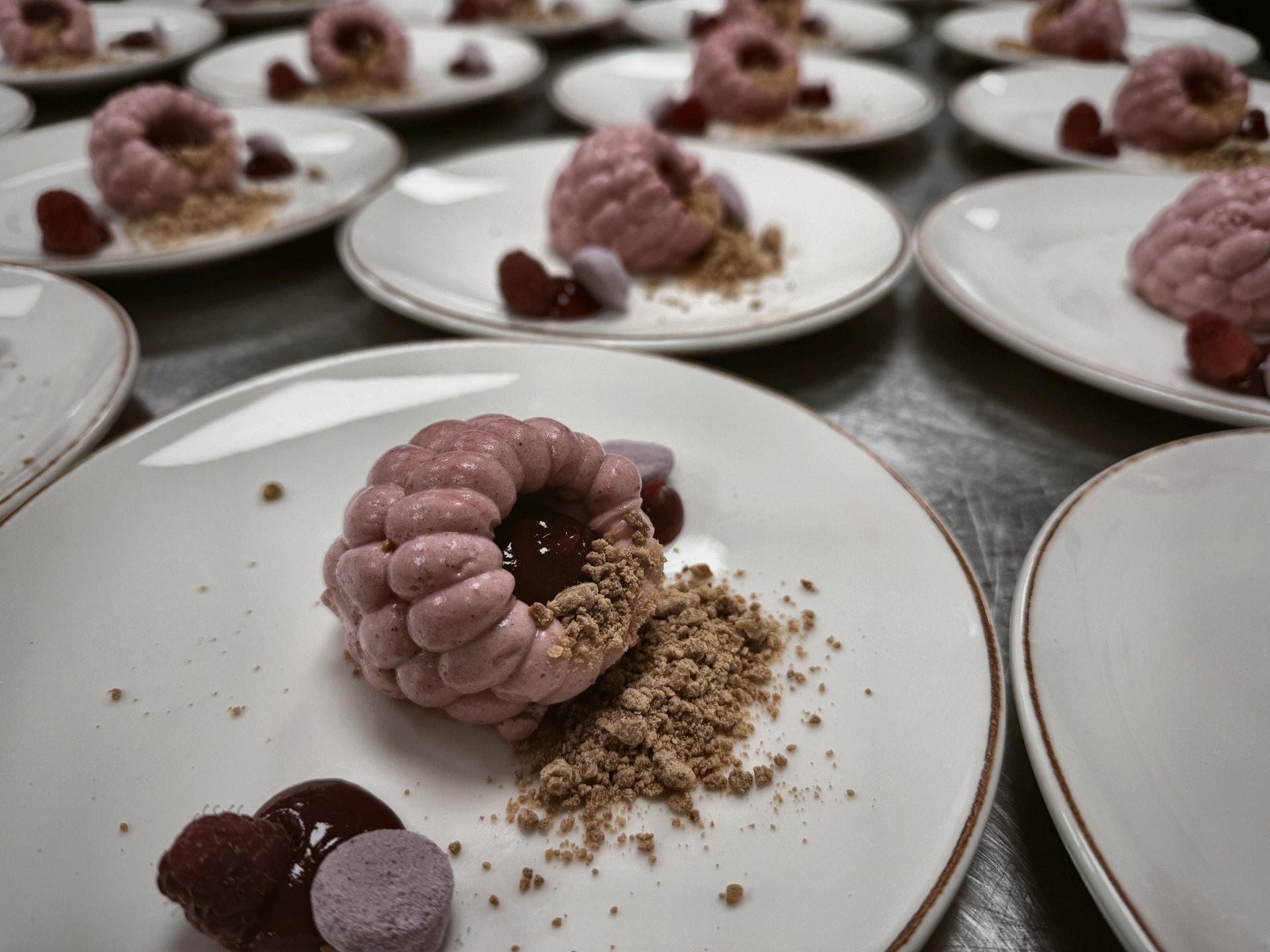 Uppdukade tallrikar med hallonmousse, syltade bär och smulad kaka på en stålbänk